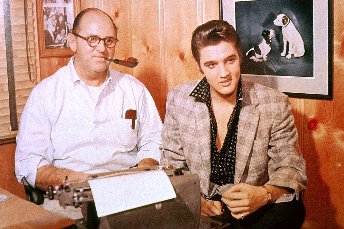 Foto de Parker, fumando cachimbo em frente a uma máquina de escrever, ao lado do jovem Elvis.