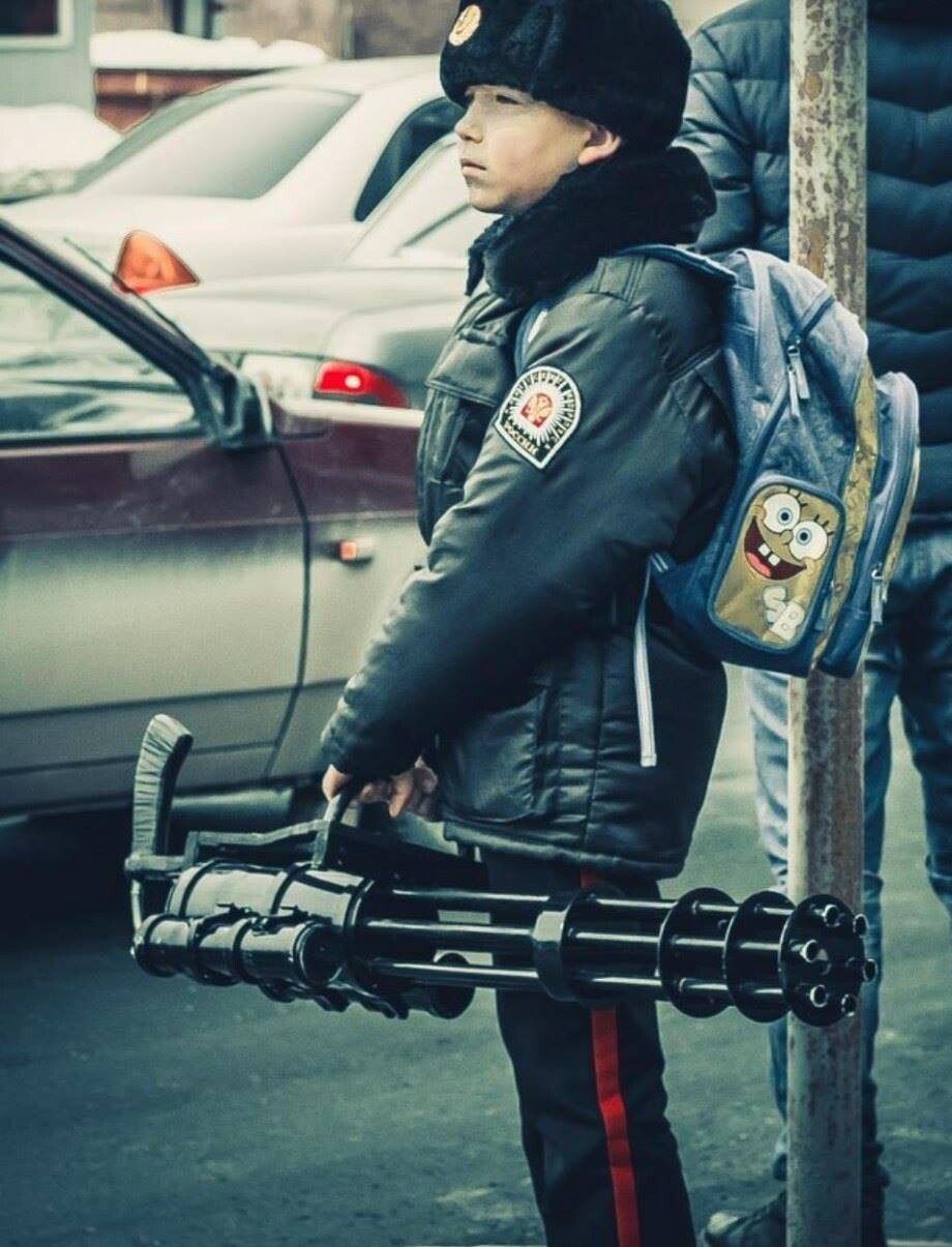 Criança com mochila colorida do Bob Esponja, uniforme militar, e arma automática de 6 canos longos