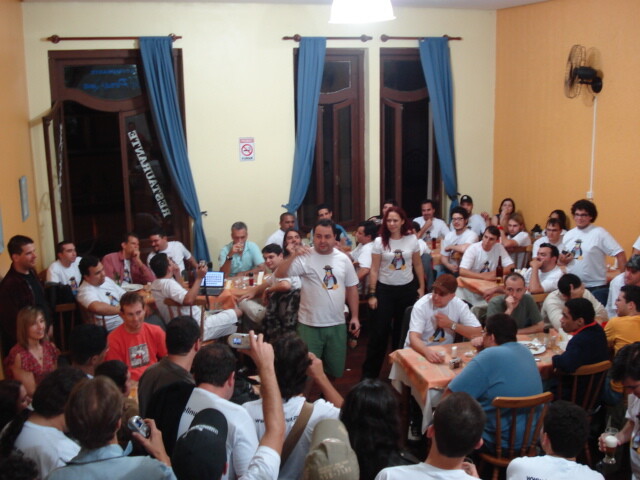 Versão (pouco) ampliada da foto que ilustra o print do link acima, mostrando algumas dezenas de entusiastas do código aberto reunidos em uma churrascaria portoalegrense, com suas camisetas indicando as respectivas afiliações.