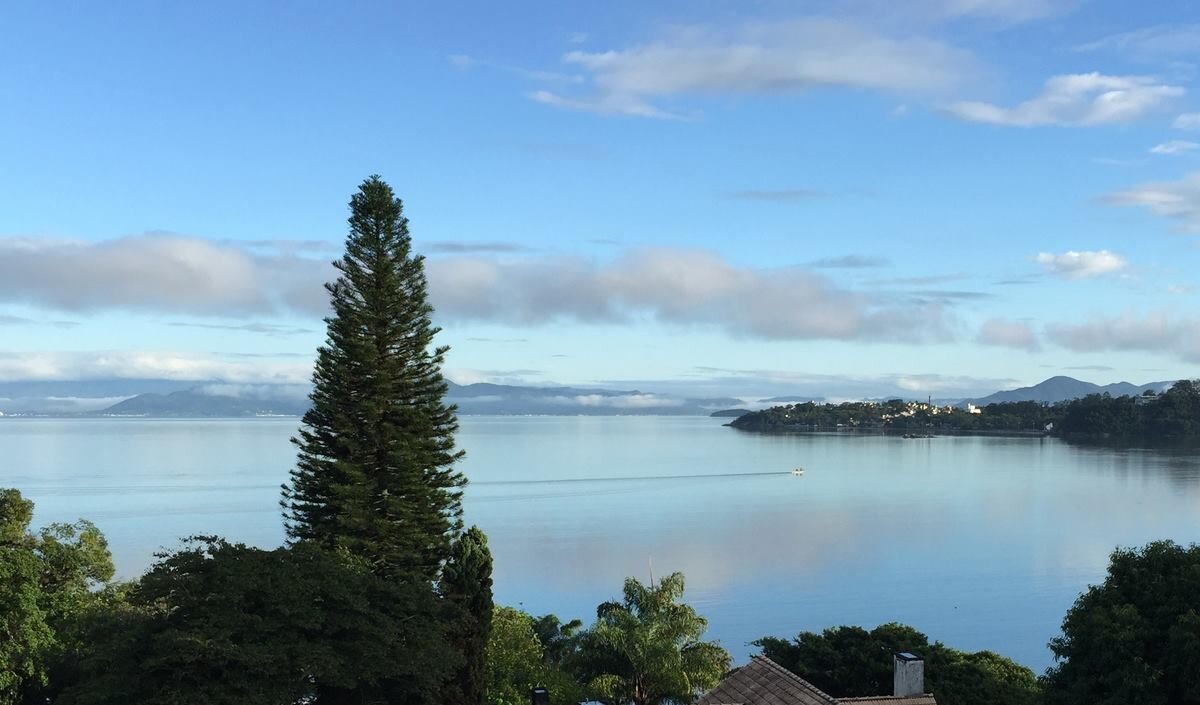 foto do céu azul com nuvens distantes, e trecho da Baía Norte de Florianópolis, com vista para o bairro Cacupé, de um lado, e para o continente, do outro.
