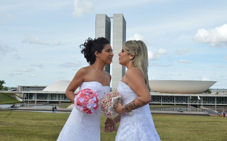 Casal celebra sua união em frente à sede do Legislativo federal, ambas de branco e com buquês