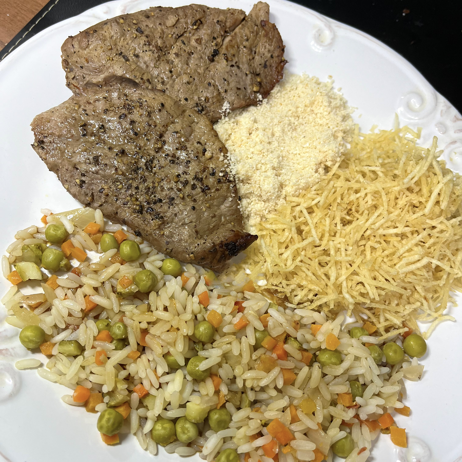 Prato servido com 2 bifinhos repletos de pimenta preta moída, e mais um arroz temperado com legumes, farofa, e batata palha