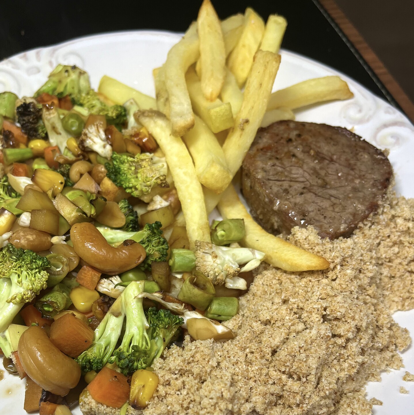 Um prato de bifinho, batata frita, farofa e muitos legumes picados, ao shoyo