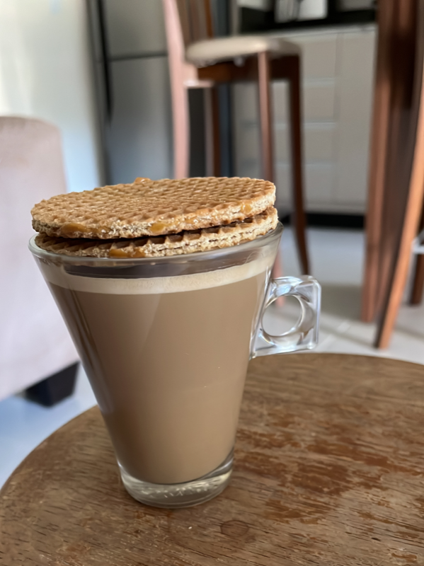 minha xícara de café com leite, em cima de uma banqueta, com 2 biscoitões em cima dela pra alcançar a consistência ideal com o calor liberado