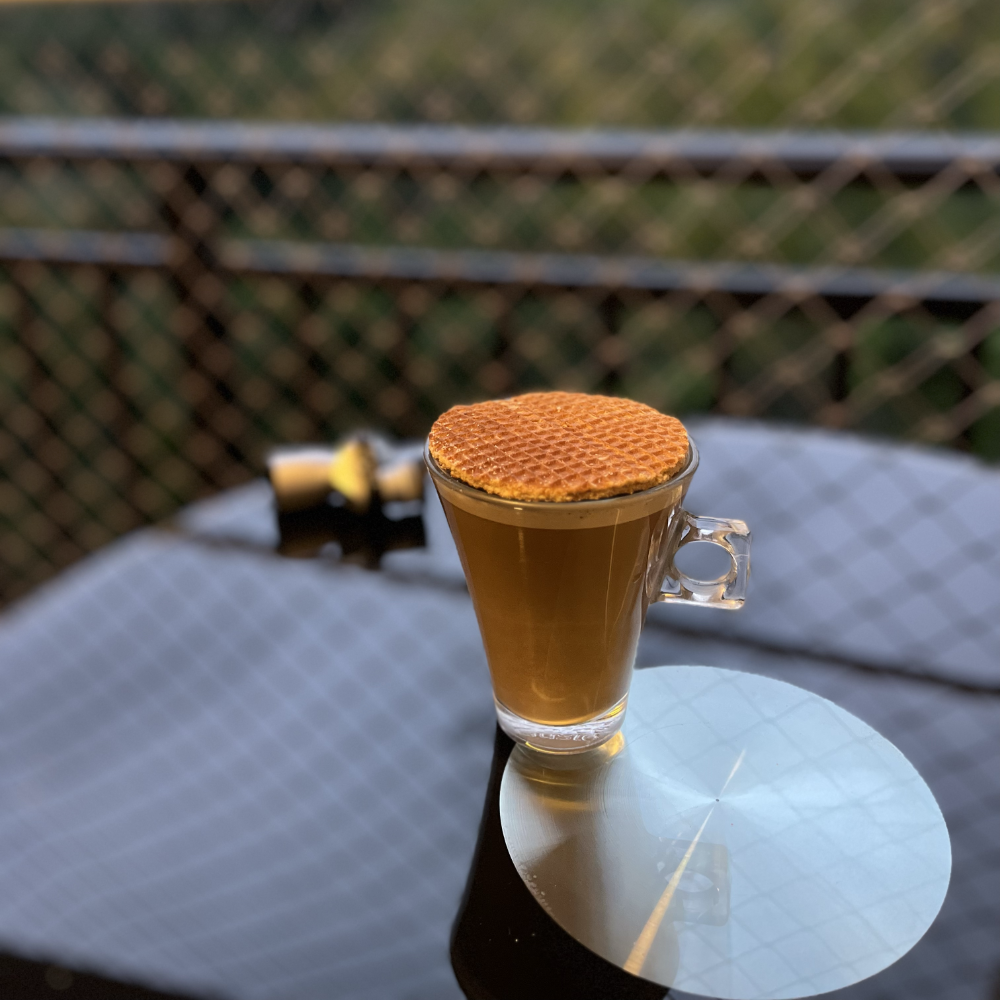 Xícara de café, com um biscoito a eclipsando, na mesinha da sacada, com o mato e a chuva ao fundo