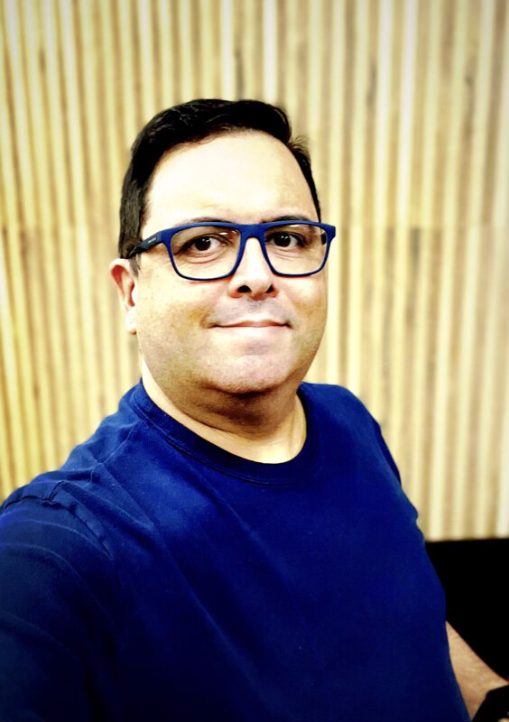 Selfie minha, com concreto texturizado ao fundo, de camiseta azul e óculos de aro azul