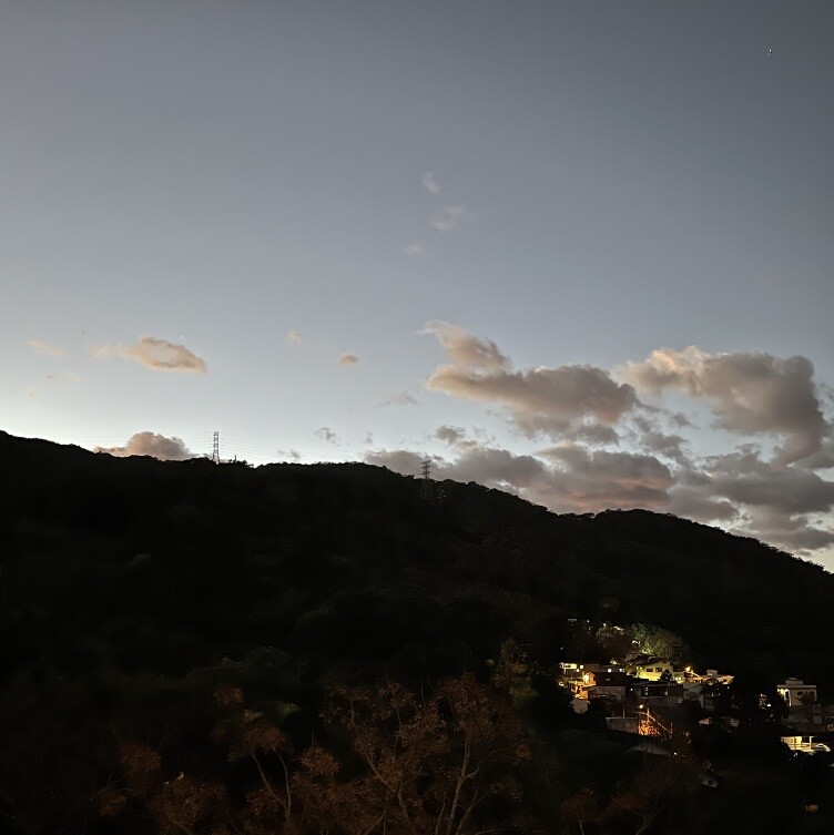 Foto do morro atrás da minha casa, ao amanhecer, com poucas nuvens no céu em tonalidade acinzentada