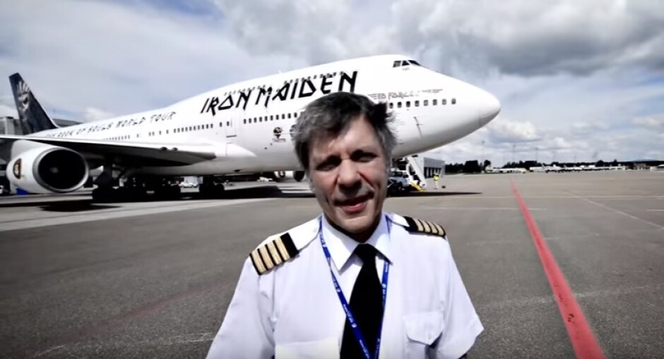 Bruce Dickinson, com traje de capitão aeronáutico, em frente à aeronave identificada com o nome do Iron Maiden