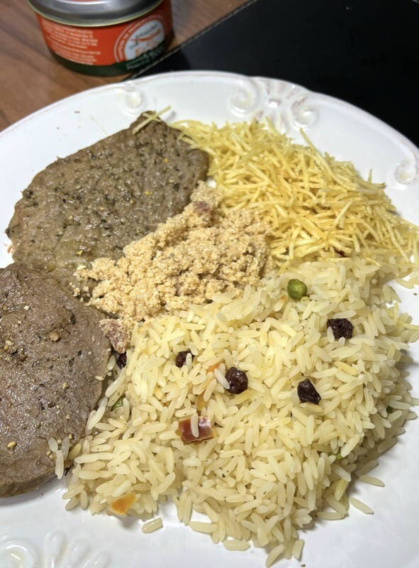 Um prato de janta servido com bife, arroz temperado, farofa e batata palha