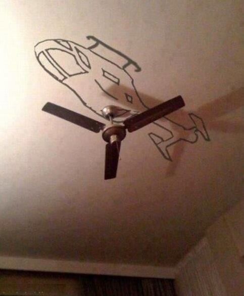 Helicóptero desenhado de cabeça para baixo num teto, tendo como hélice as pás de um ventilador de teto