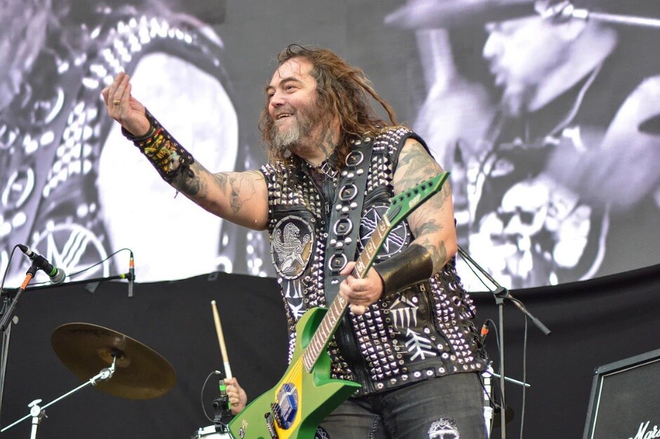 Max Cavalera sorri no palco, com uma guitarra nas cores do Brasil
