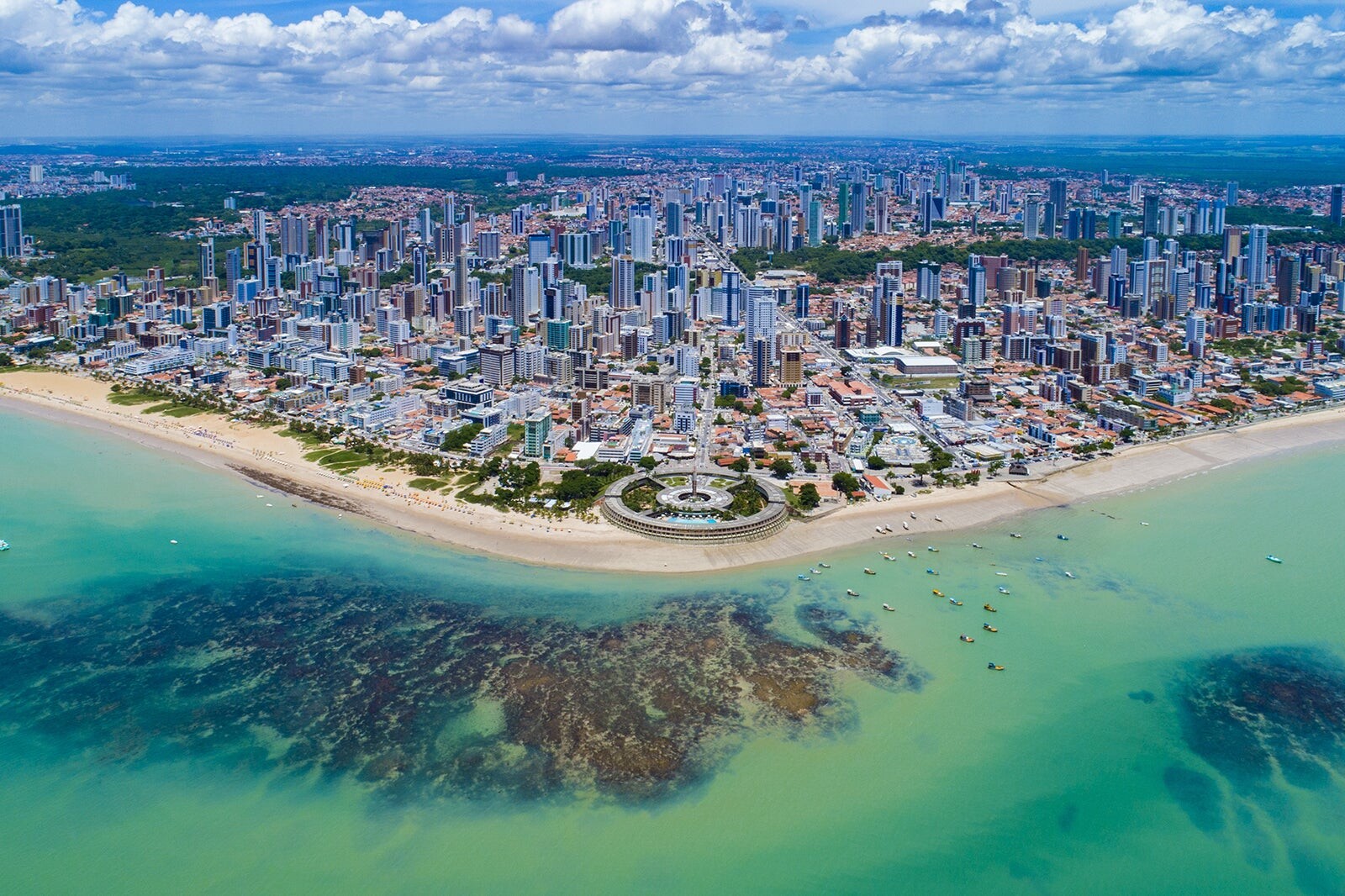 Foto aérea da região urbanizada de João Pessoa, vista a partir do oceano, incluindo trecho de praia e o céu com nuvens