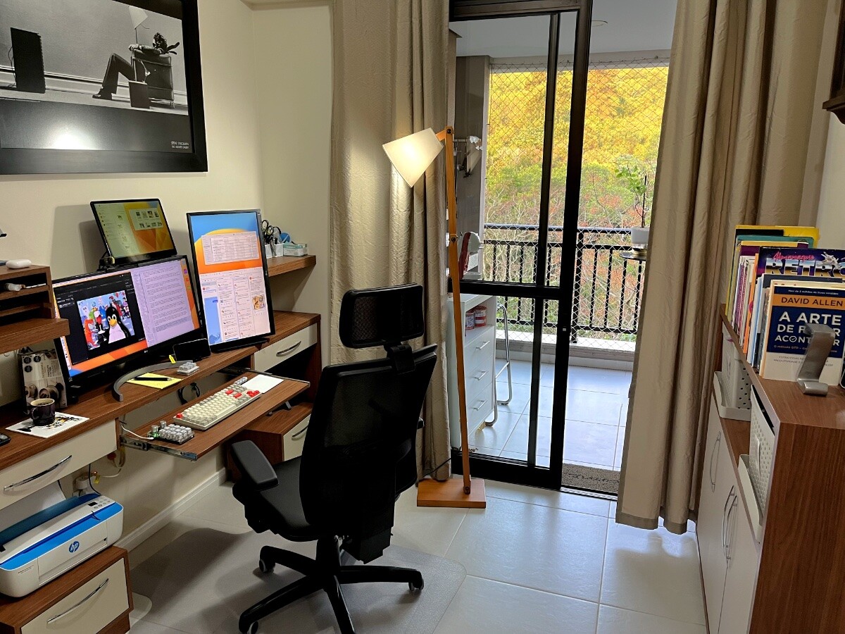 Foto do meu escritório, mostrando a bancada com 3 monitores, sendo 2 deles (à esquerda, empilhados) na horizontal, e o outro, à direita, na vertical. <br><br>O monitor novo é o do alto à esquerda, e tem aproximadamente metade da largura do outro monitor que está abaixo dele.