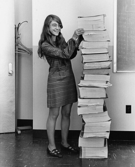 Célebre foto em preto e branco de Margaret Hamilton ao lado de uma pilha de listagens, mais alta que ela, dos sistemas de bordo do programa Apollo