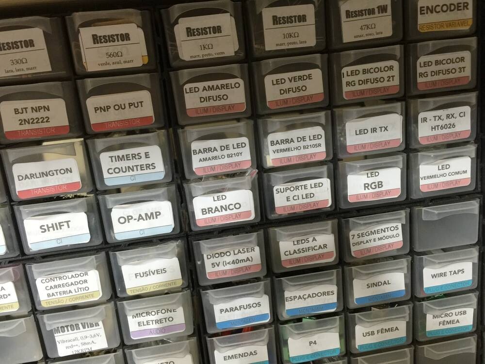 Cerca de 40 gavetinhas de miudezas, com etiquetas coloridas identificando itens como transistor 2N2222, resistor de 560 ohms, led amarelo difuso, sindl, microfone eletreto e muito mais