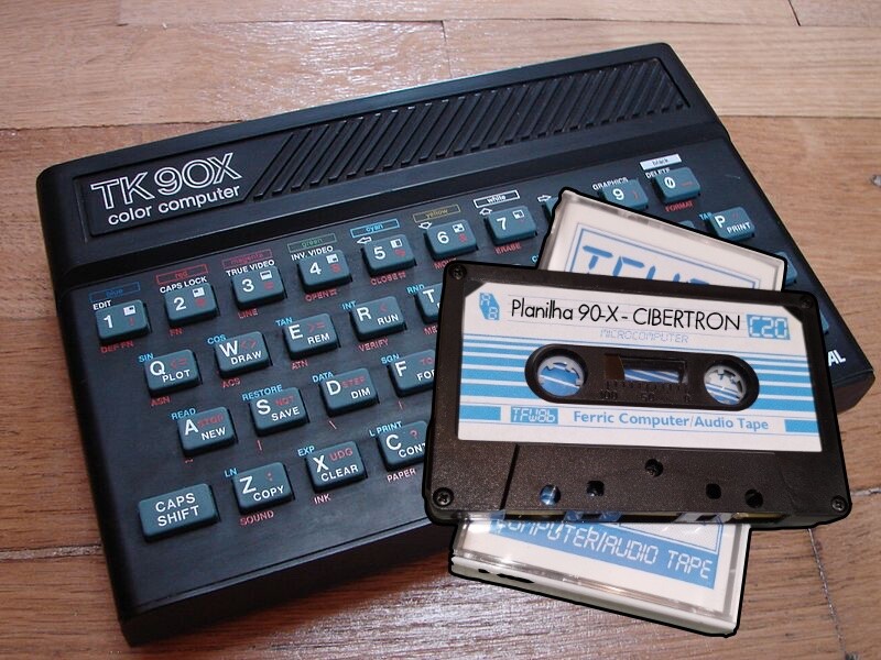 Fita K7 de 20 minutos identificada como Planilha 90-X, sobre uma foto de um TK90X 