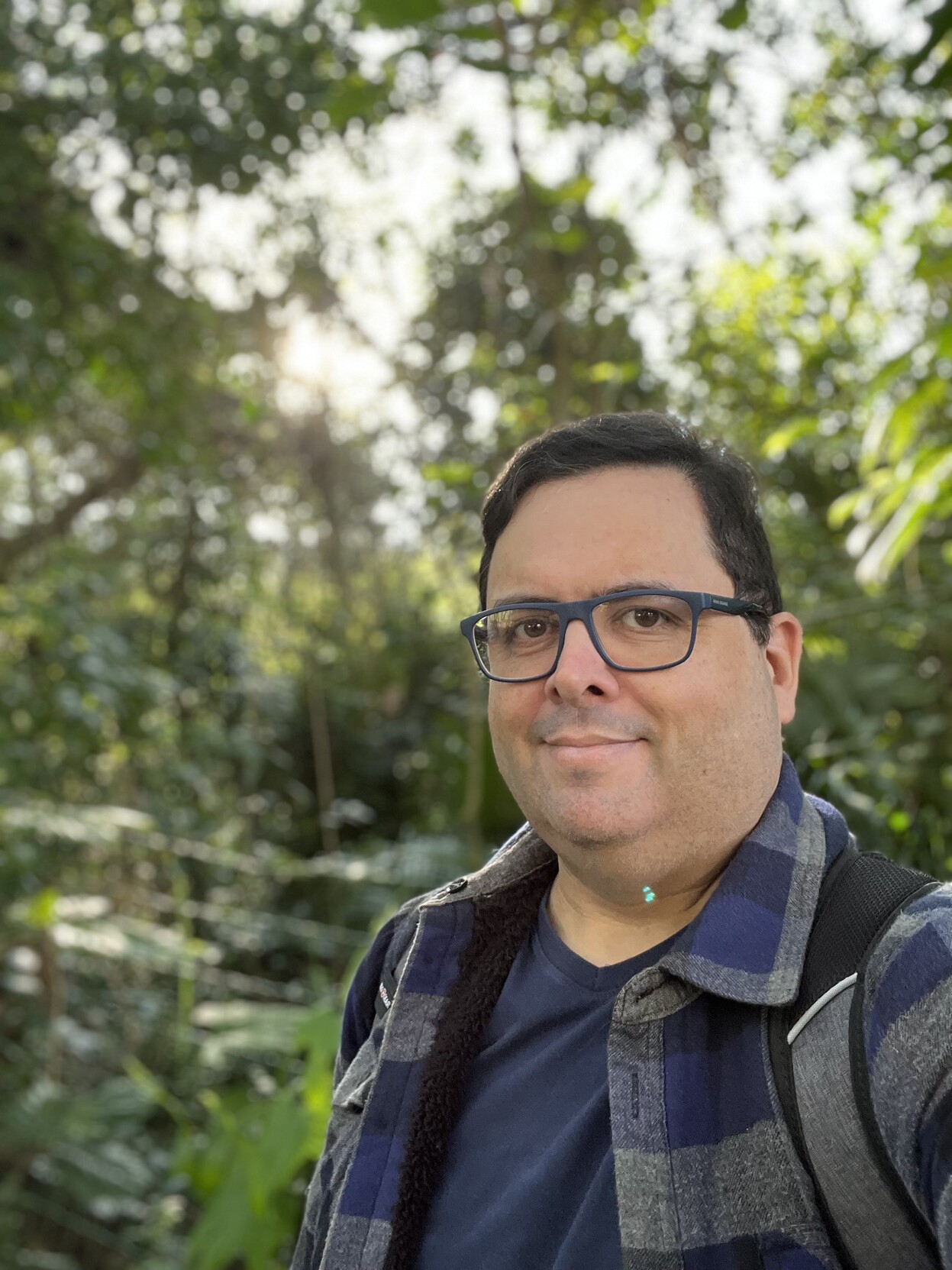 Selfie minha, de blusa grunge azul, camiseta azul e óculos de armação azul, em meio à vegetação nativa ensolarada 