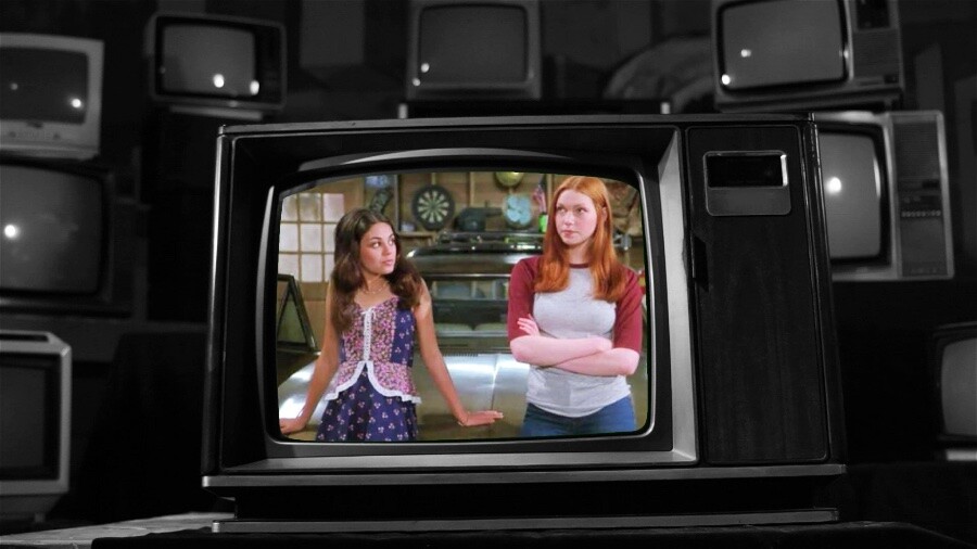 As personagens Jackie Burckhart e Donna Pinciotti conversam na garagem, sentadas sobre o capô do Vista Cruiser