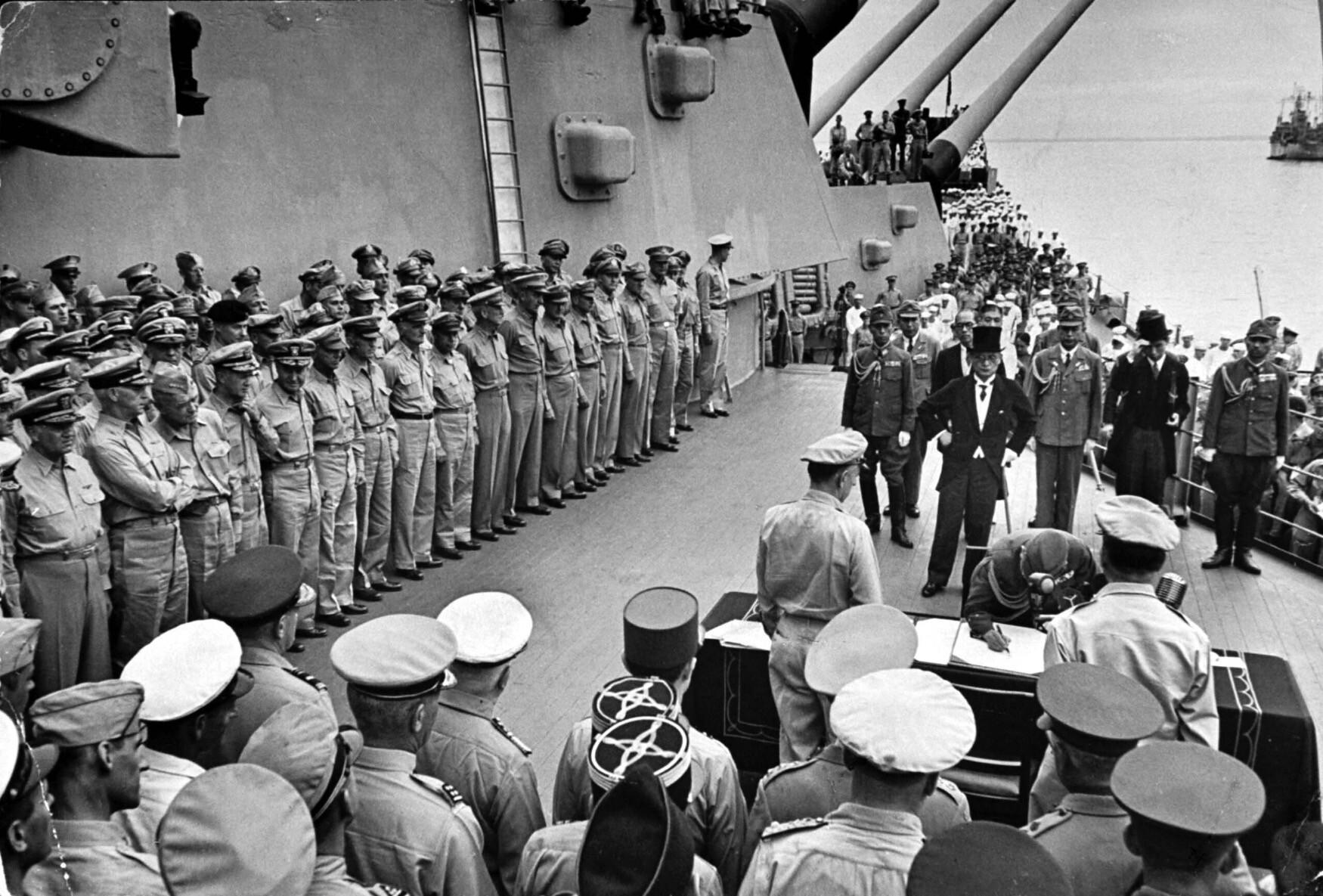 Oficiais americanos em formatura no convés do USS Missouri enquanto a delegação japonesa, incluindo o ministro das Relações Exteriores Mamoru Shigemitsu (de cartola), observava o general Yoshijiro Umezu assinar os documentos oficiais de rendição, encerrando a Segunda Guerra Mundial. 
