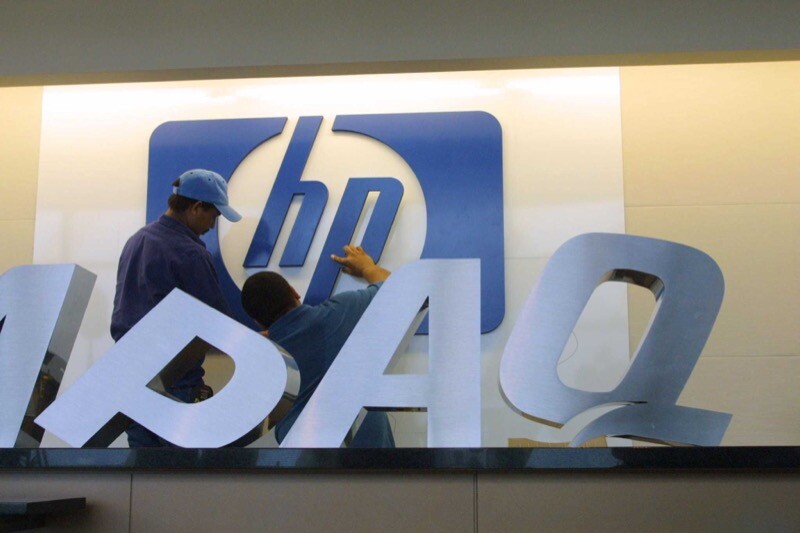 Trabalhadores removem logo da Compaq e instalam o da HP em uma parede interna