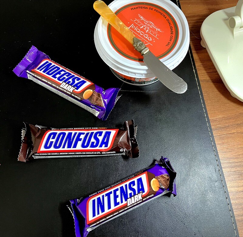 3 chocolates Snickers sobre a minha mesa de café, com rórulos temáticos dizendo: <br>- INDECISA DARK<br>- CONFUSA<br>- INTENSA DARK