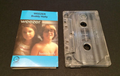 K7 single de Buddy Holly, do Weezer, com capa contendo foto de uma criança com óculos no estilo do Buddy Holly, e outra que lembra o penteado de Mary Tyler Moore