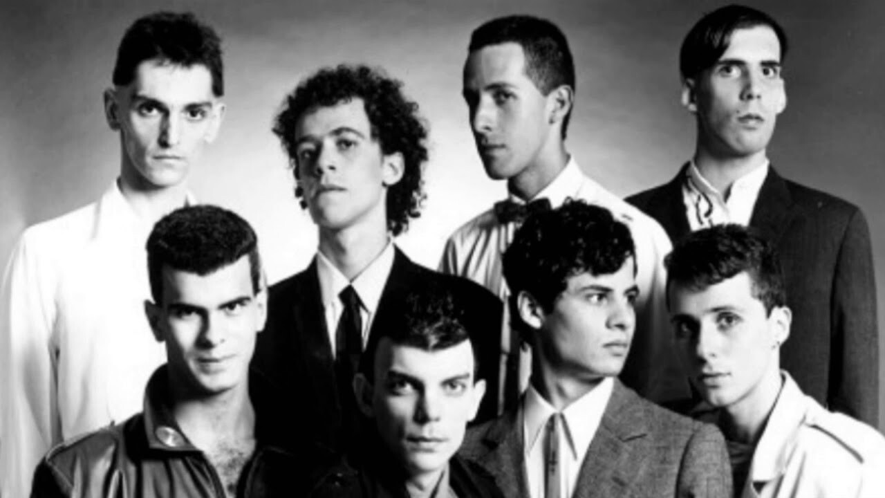 Nando Reis e os demais Titãs em foto de 1989, em preto e branco, em trajes sociais e com expressões sisudas