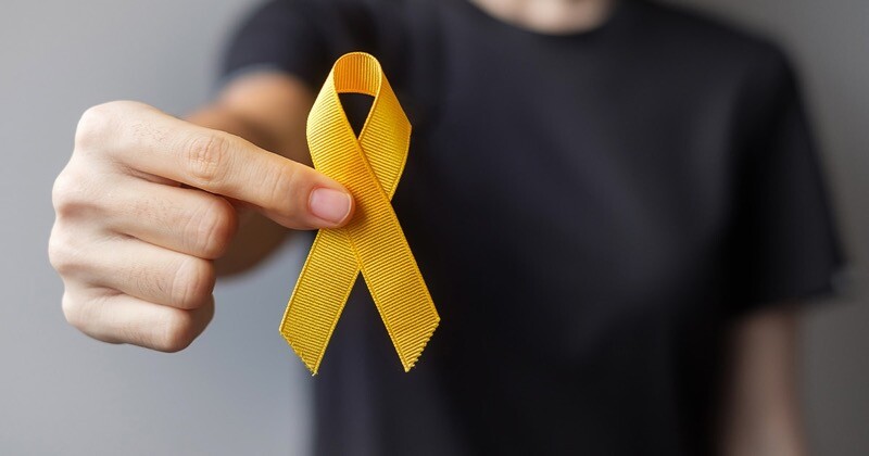 pessoa com camisa preta e rosto fora do enquadramento segura um laço amarelo de fita