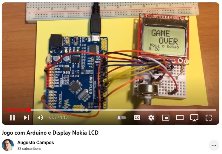 Sobre um post-it amarelo, um arduino (clone, chamado Uno Plus) conectado a um display de vídeo monocromático exibindo a expressão “Game Over - mova o botão“. Ao seu lado, componentes eletrônicos em uma mini-protoboard, e uma mão toca o eixo de um potenciômetro