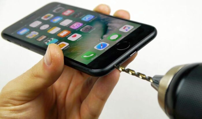Uma furadeira posicionada no exterior de um iPhone 7, onde a porta de fone de ouvido de 3,5mm estaria