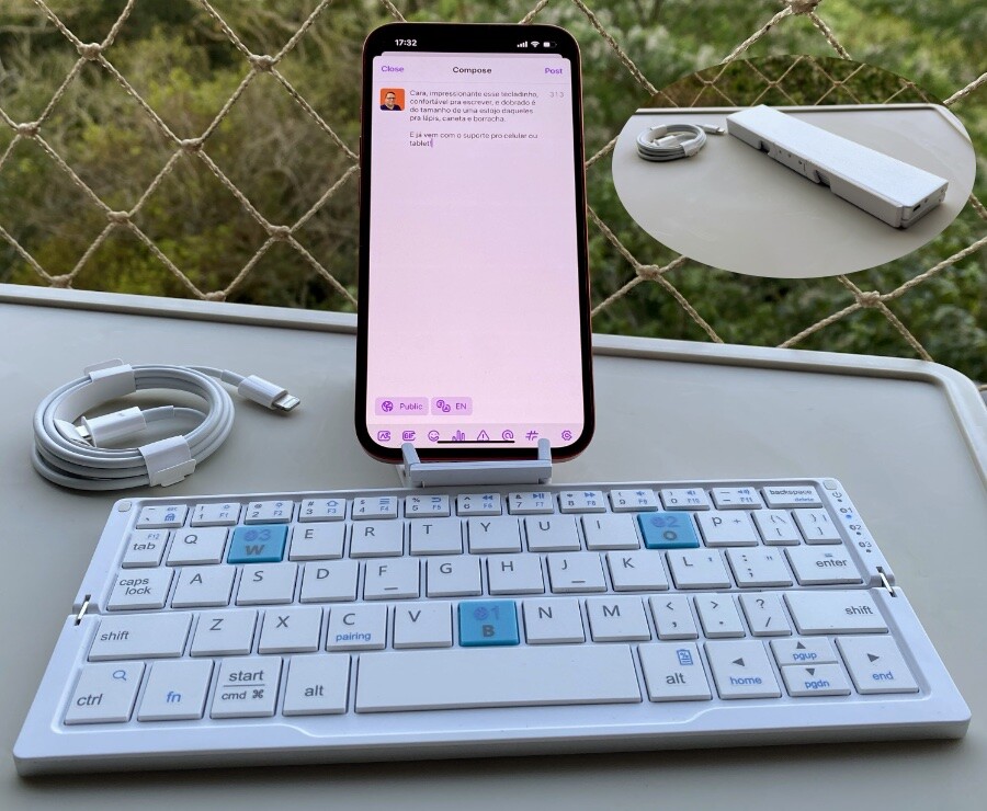 Foto de um teclado de pequeno porte, com um celular encaixado no suporte anexo, editando o texto deste toot. No detalhe, uma foto menor mostrando o teclado dobrado, em formato retangular de 20 x 4,5cm, e 1,5cm de altura