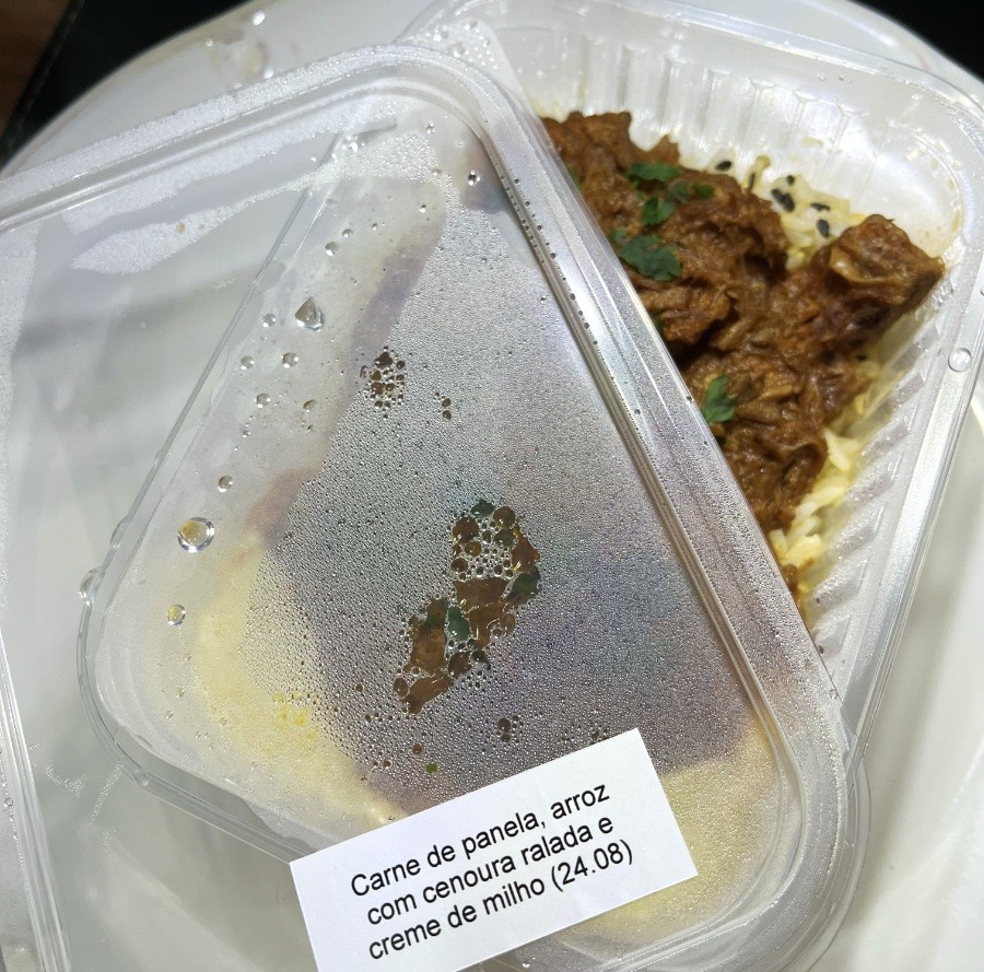 Uma quentinha com etiqueta onde está escrito: carne de panela, arroz com cenoura ralada e creme de milho