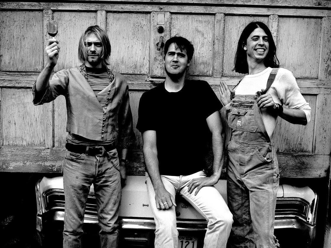 PIC: Os integrantes do Nirvana posam para foto em cenário de garagem, em 1993. Da esquerda para a direita: Kurt Cobain, Krist Novoselic, Dave Grohl. Foto de Anton Corbijn.<br>