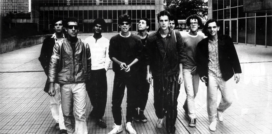 A primeira formação do Titãs, no início dos anos 80, lado a lado em frente a um prédio, enm foro em preto e branco. <br><br>Da esquerda para a direita, atrás: Arnaldo Antunes, André Jung, Tony Bellotto, Sérgio Britto e Nando Reis. <br><br>À frente: Marcelo Fromer, Branco Mello, Ciro Pessoa e Paulo Miklos.<br>