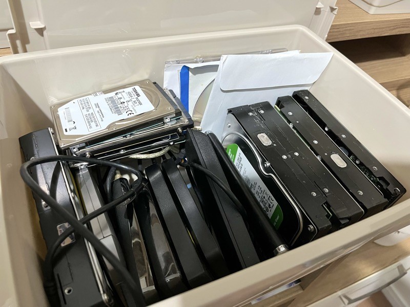 Uma caixa cheia de HDDs grandes, pequenos, internos, externos, SSDs e alguns CDs
