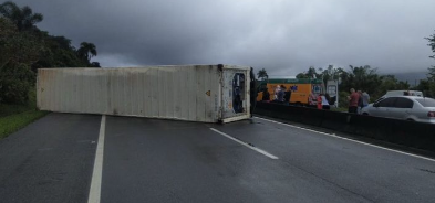 Carreta tombada de um lado da pista, e fila de carros visível no lado oposto