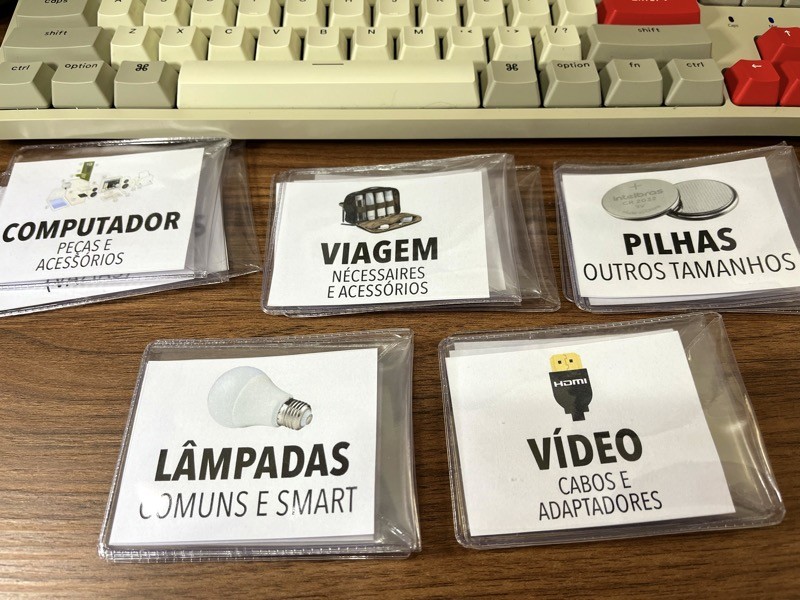 5 pilhas de etiquetas impressas, com ícones e nomes como PILHAS, LÂMPADAS, VÍDEO e mais.