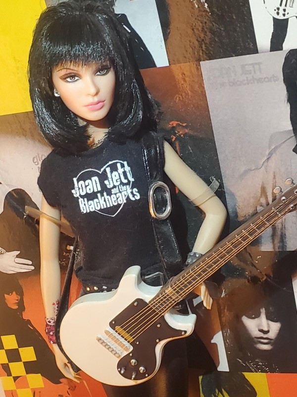 A Barbie da Joan Jett, com roupa preta, camiseta da banda Joan Jett and the Blackhearts, e guitarra
