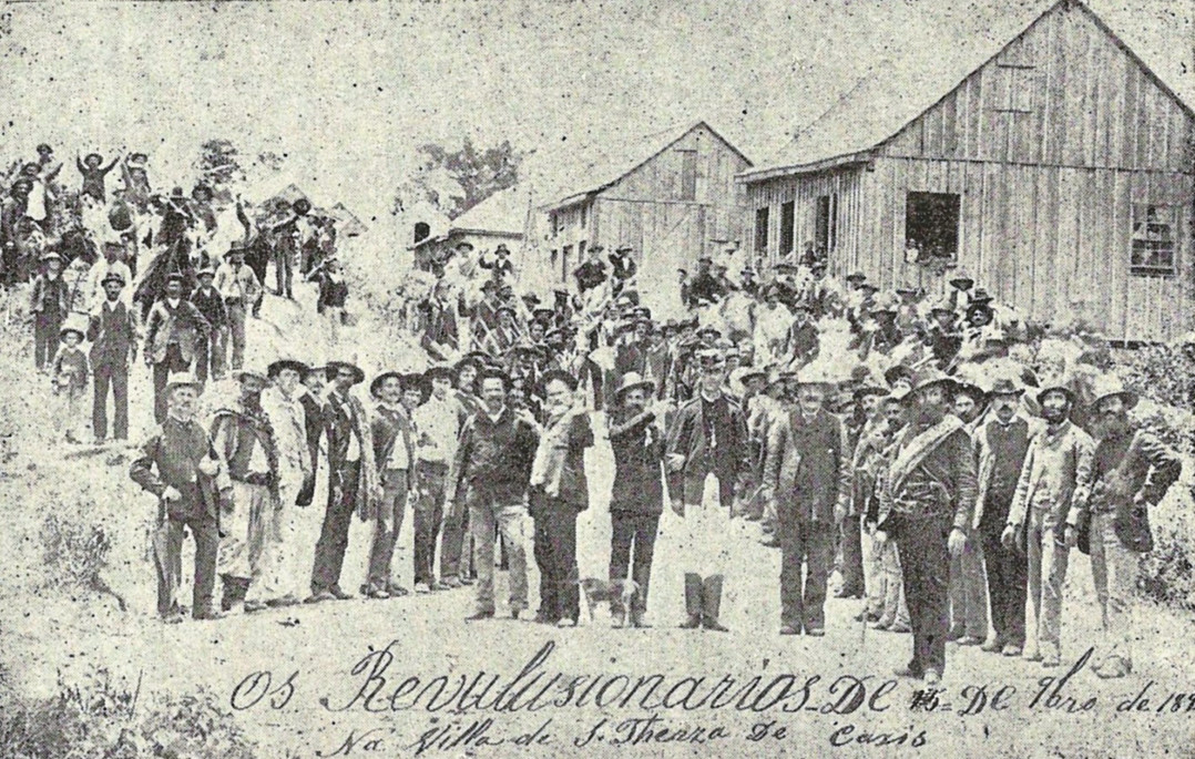 Foto em preto e branco dos líderes da primeira Revolta dos Colonos, em 1891. No primeiro plano, ao centro, de farda, o delegado de polícia Francisco Januário Salerno, e à extrema direita, com uma faixa ao peito, o chefe dos revoltosos, Afonso Amabile.<br>