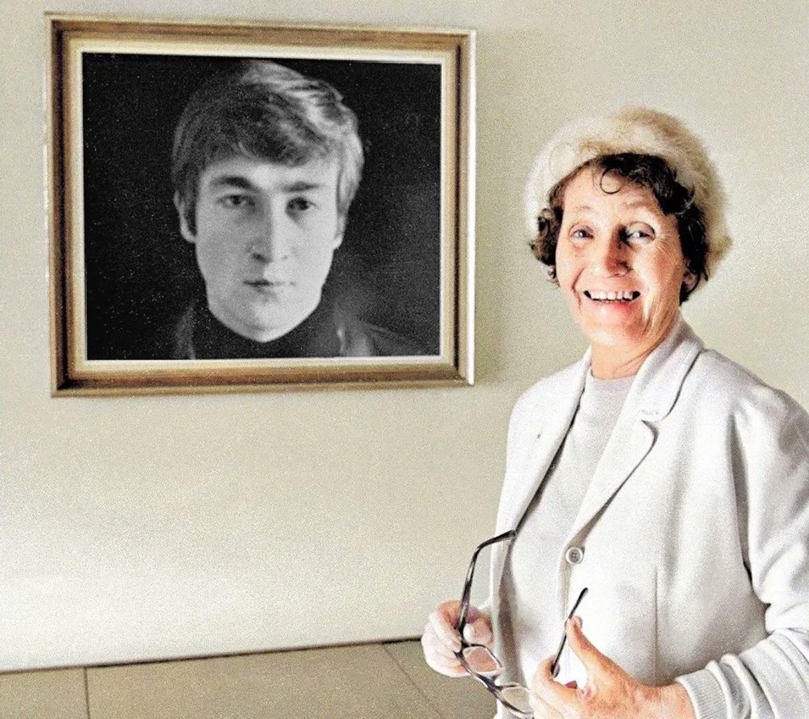 Mimi Smith posa junto a uma foto em preto e branco de John Lennon