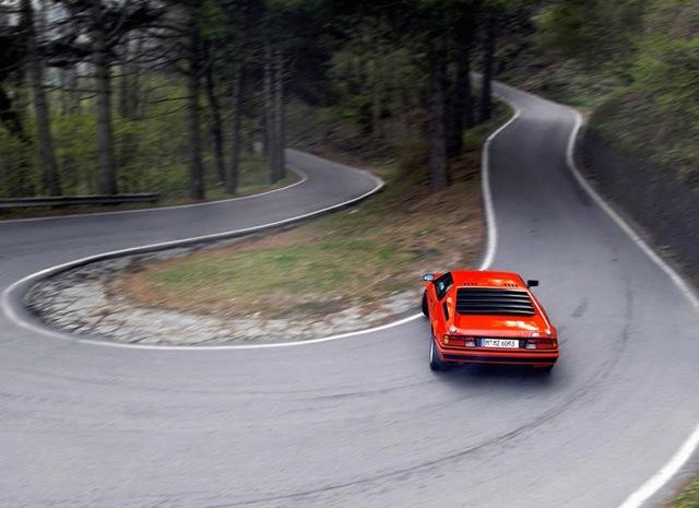 Um carro esportivo vermelho com linhas clássicas fazendo, de lado, uma curva fechada em uma rodovia de montanha