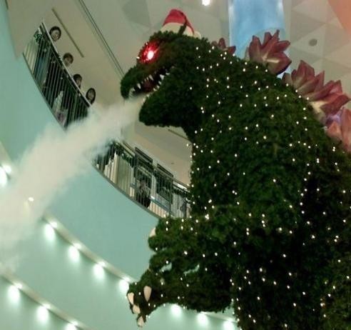 Uma árvore de natal de shopping, no formato do godzilla, com olhos brilhantes e soprando fumaça branca