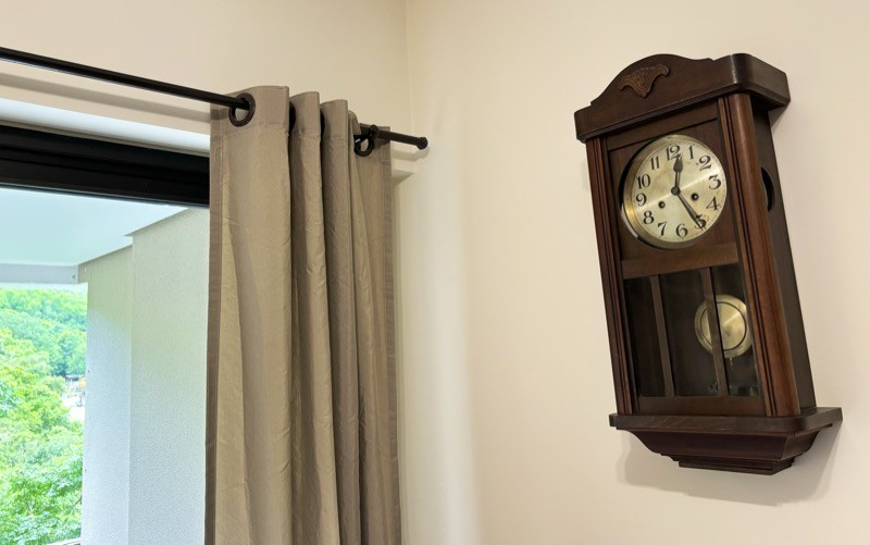 Um relógio de parede, com gabinete em madeira envidraçada. marcando 12h25min