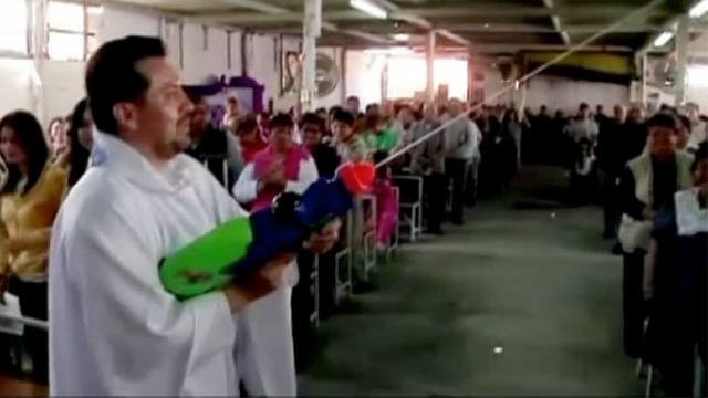 Padre usa uma colorida metralhágua para lançar jatos de água benta na direção de sua congregação
