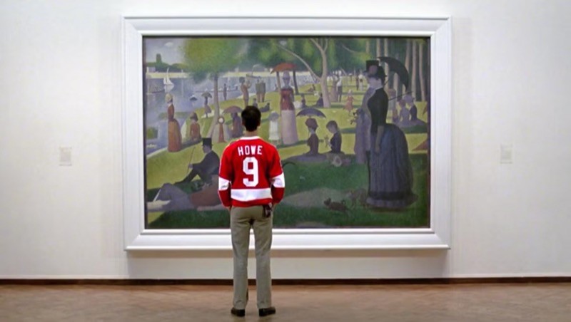 Cameron Fry, com uma camisa vermelha de time esportivo (número 9, escrito “HOWE“), de costas para a câmera, com as mãos nos bolsos da calça, olha para a tela Uma Tarde de Domingo na Ilha de Grande Jatte, de Seurat, em uma parede de museu.<br>