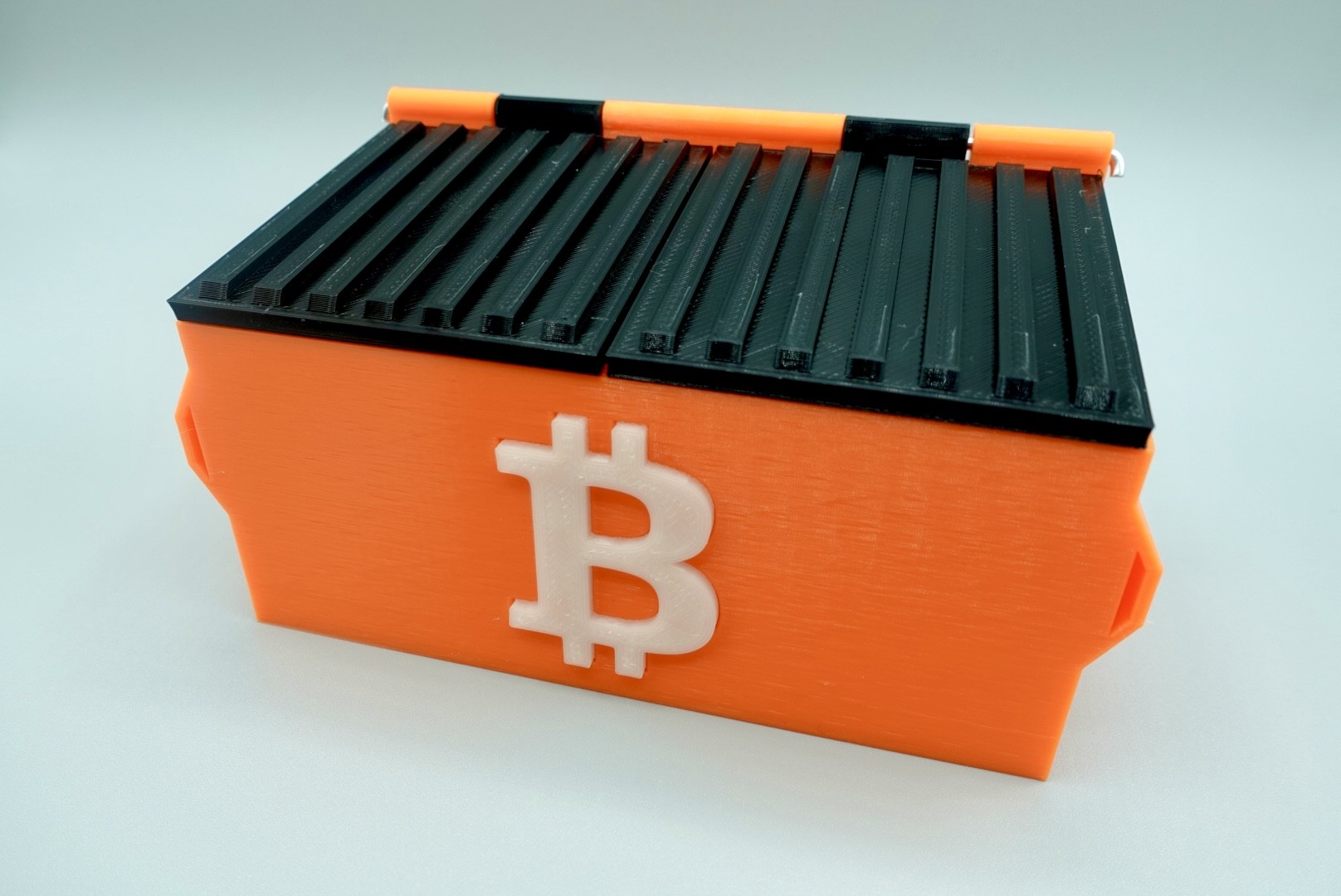 Um estojo em formato de container de lixo, com o logotipo do Bitcoin.