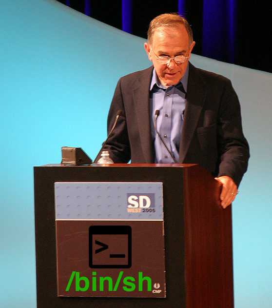 Steve Bourne faz uma palestra em 2005. No seu púlpito foi sobreposto um ícone da shell e o caminho /bin/sh
