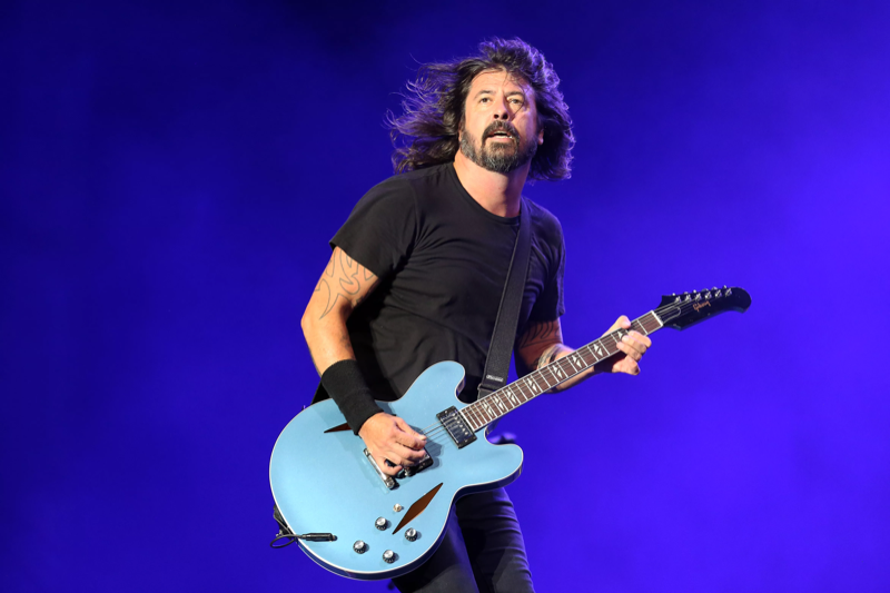 Dave Grohl no palco, com uma guitarra azul, e com cenário azul ao fundo