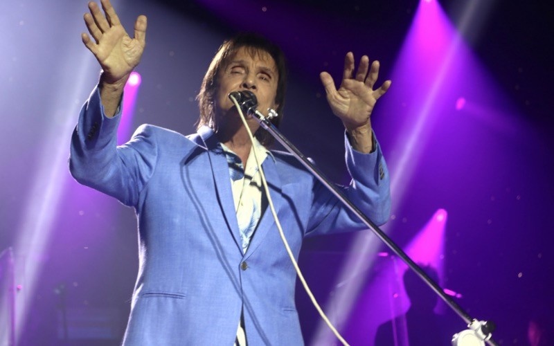 Com braços erguidos e as duas mãos espalmadas, Roberto Carlos gesticula de olhos fechados no palco.