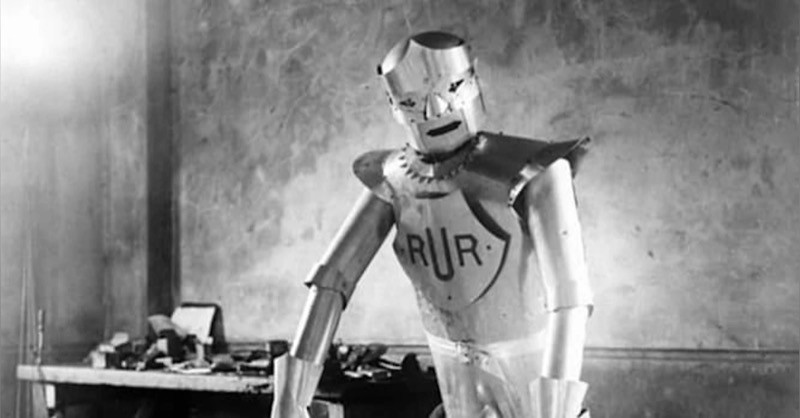 Ator interpreta um robô com o logotipo da empresa RUR, em foto em preto e branco